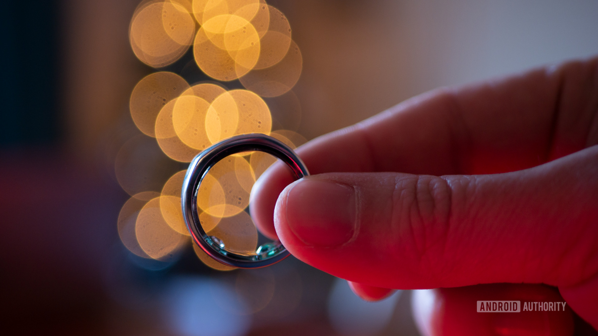 用户握有一个ourea ring 2，这是睡眠跟踪器手表的一个很好的替代品，在模糊的圣诞灯前，