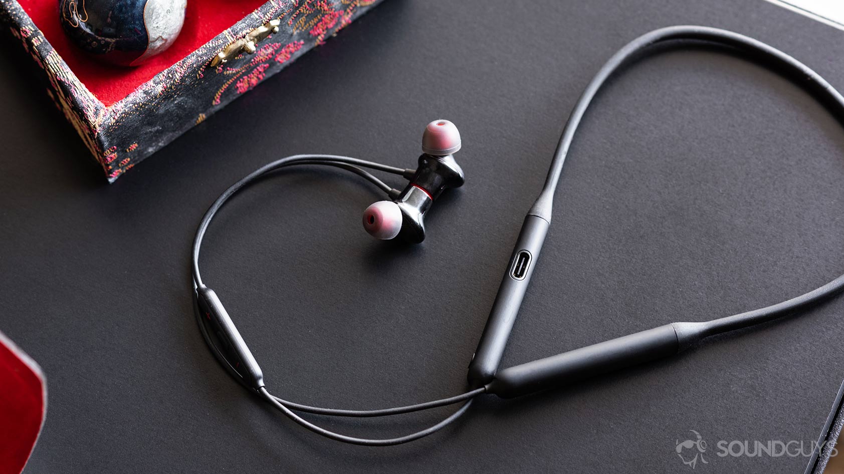 OnePlus子弹无线2：耳塞和颈带的完整图像，电缆在黑色桌子上弯曲。