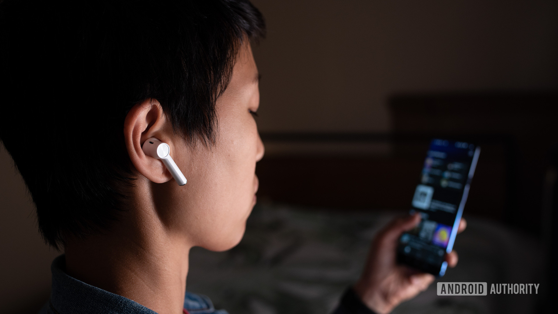 一位妇女在OnePlus 7智能手机上看Spotify的女性穿着的OnePlus Buds真实无线耳塞（白色）的图片。