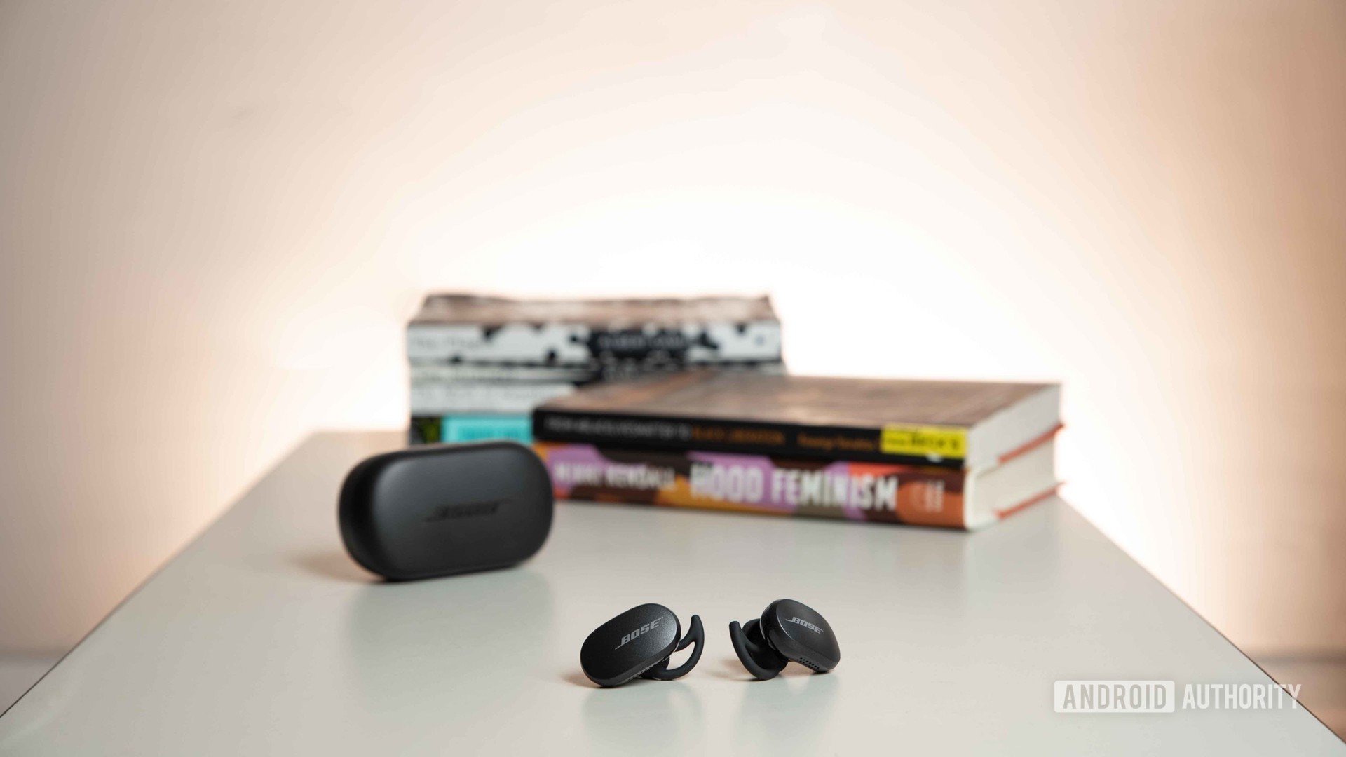 Bose Quietcomfort耳塞噪音消除了真正的无线耳塞，在桌子上和一堆书籍前的充电箱外面休息。