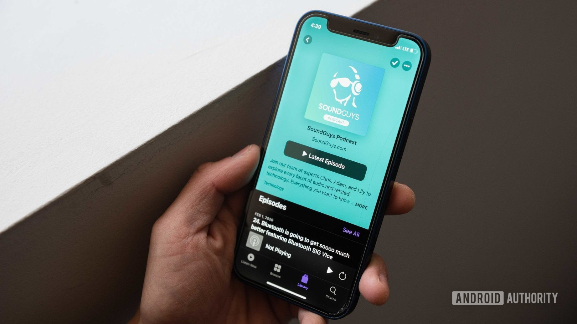 一只手拿着iPhone 12 mini，其中包含Apple Podcasts应用程序打开的Soundguys Podcast页面。