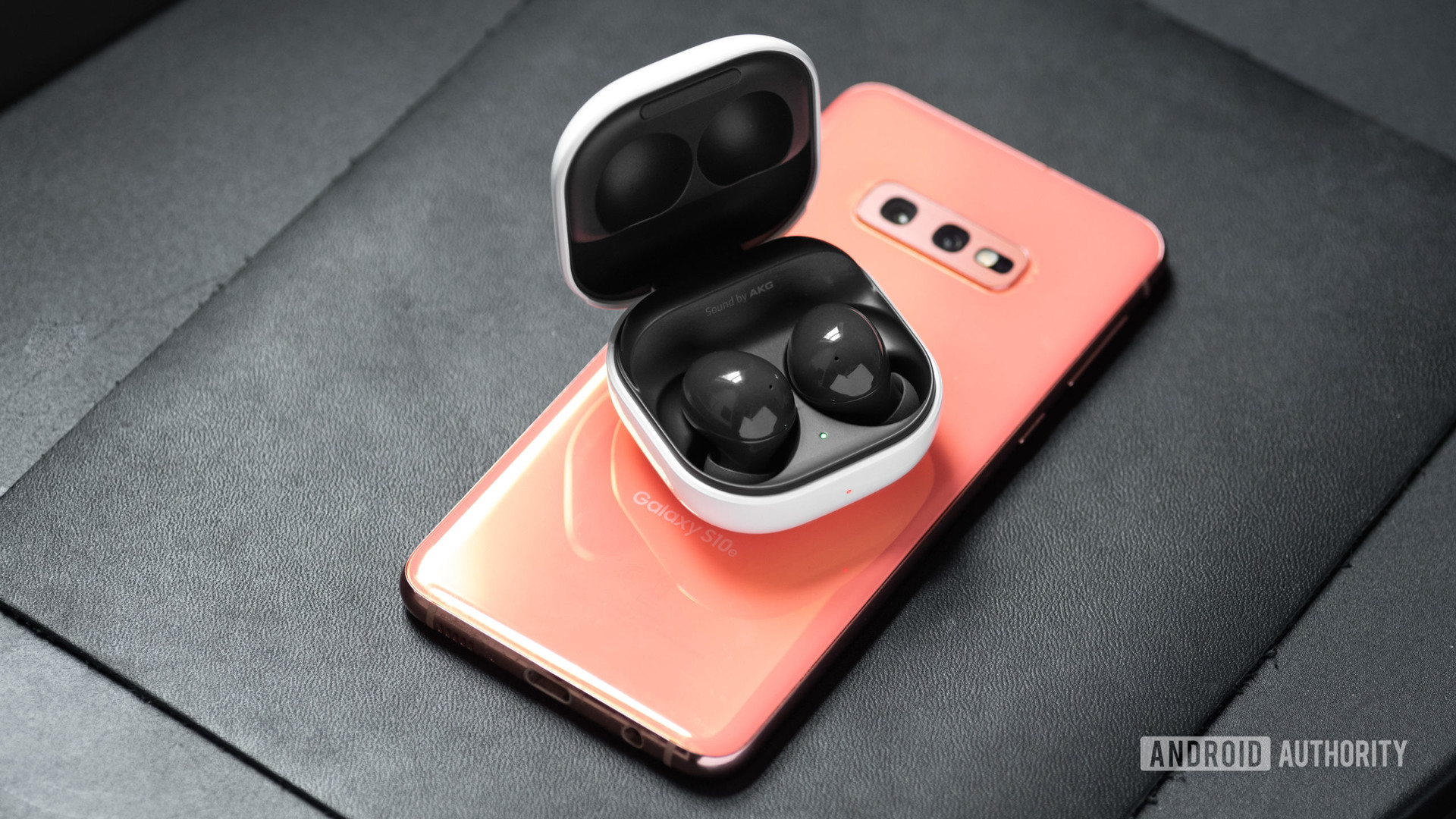 三星Galaxy Buds 2在三星Galaxy S10E智能手机的粉红色的开放充电箱中，在打开充电箱中取消真正的无线耳机。