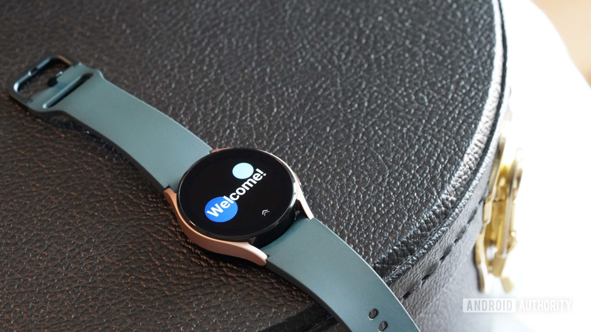 三星Galaxy Watch 4放在黑色皮箱上，显示了手表欢迎屏幕。