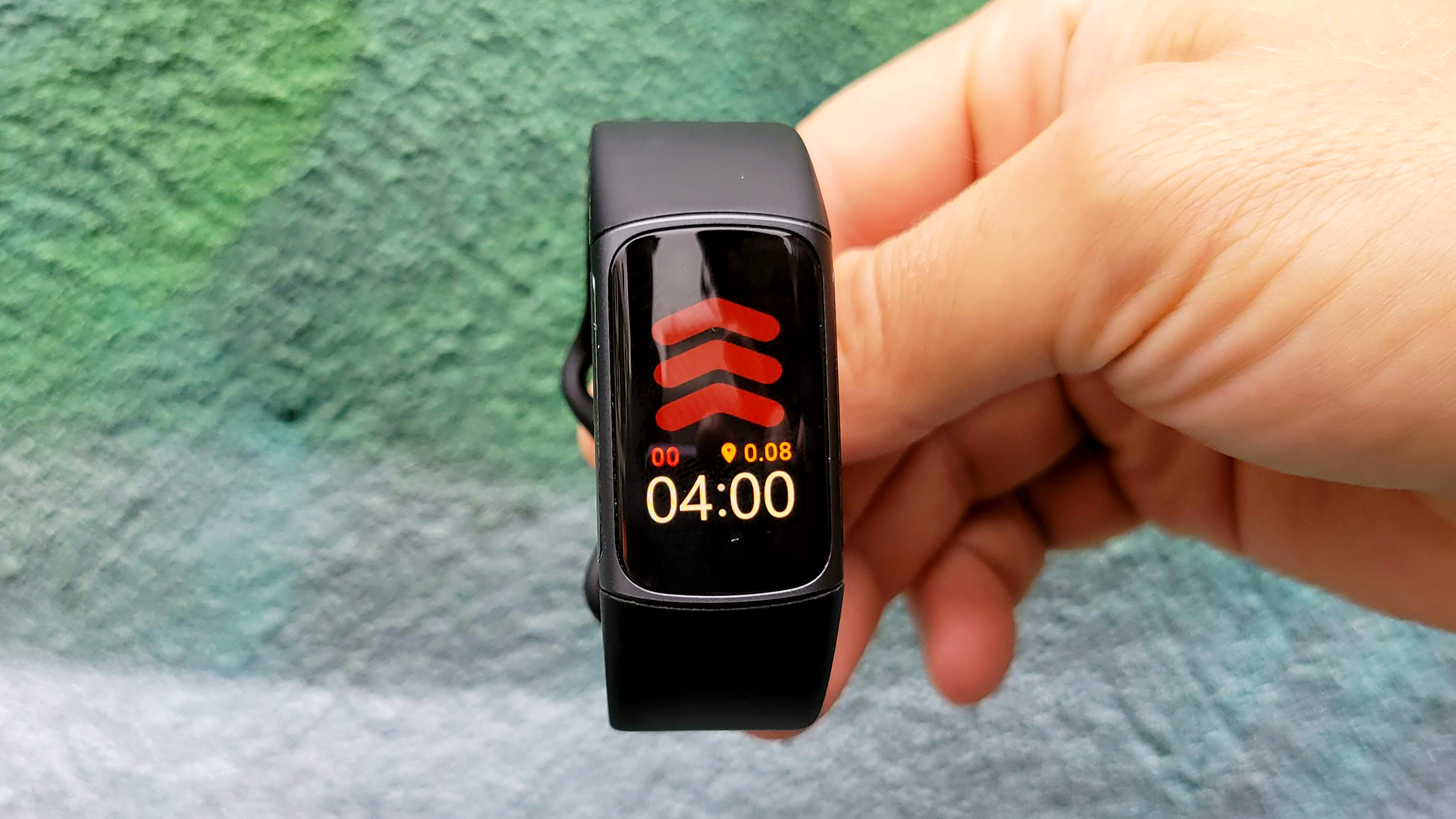 用户在绿色混凝土墙面前手持Fitbit Charge 5。