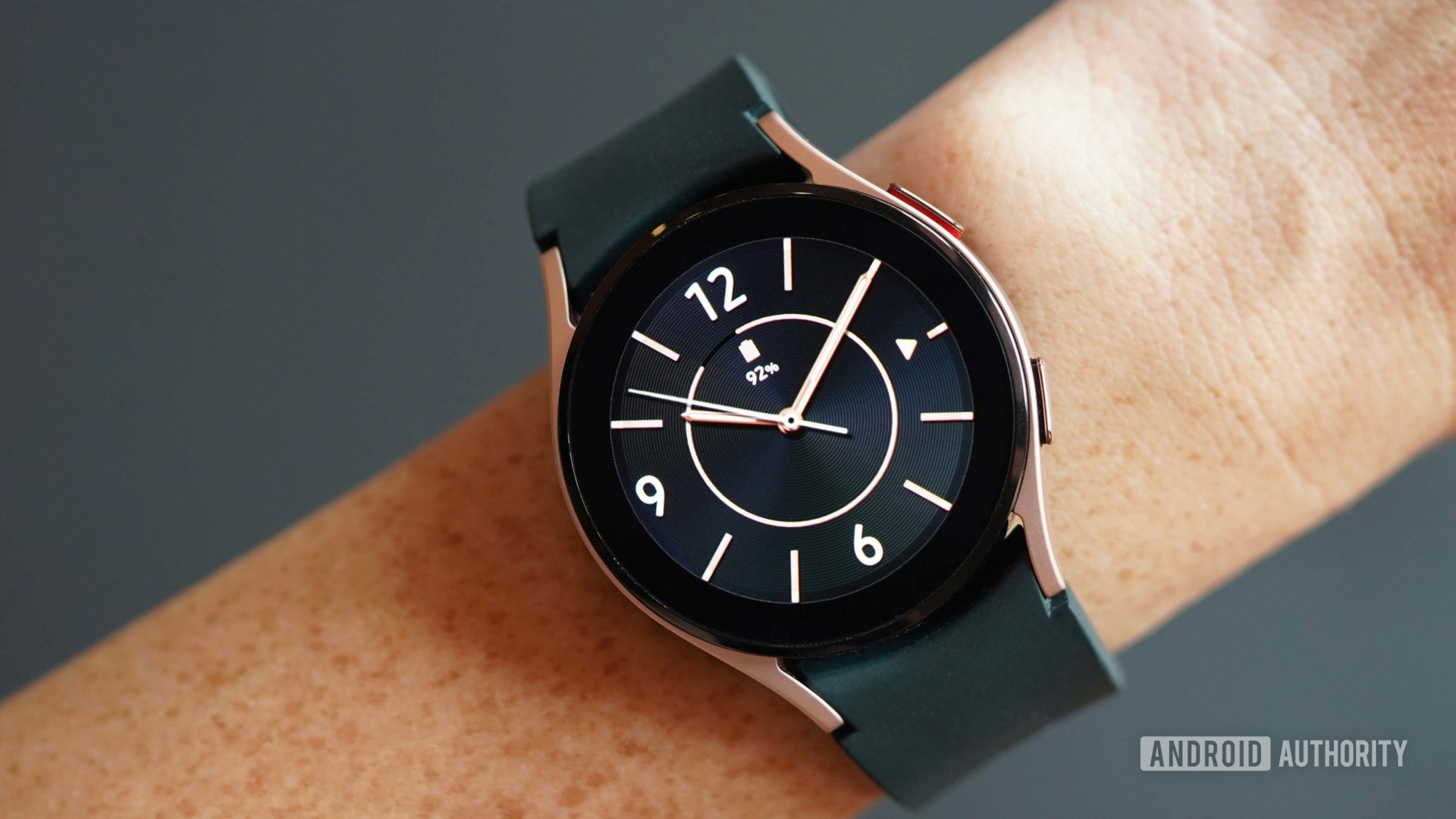 雌性手腕上的Galaxy Watch 4显示黑色和玫瑰金模拟表脸。