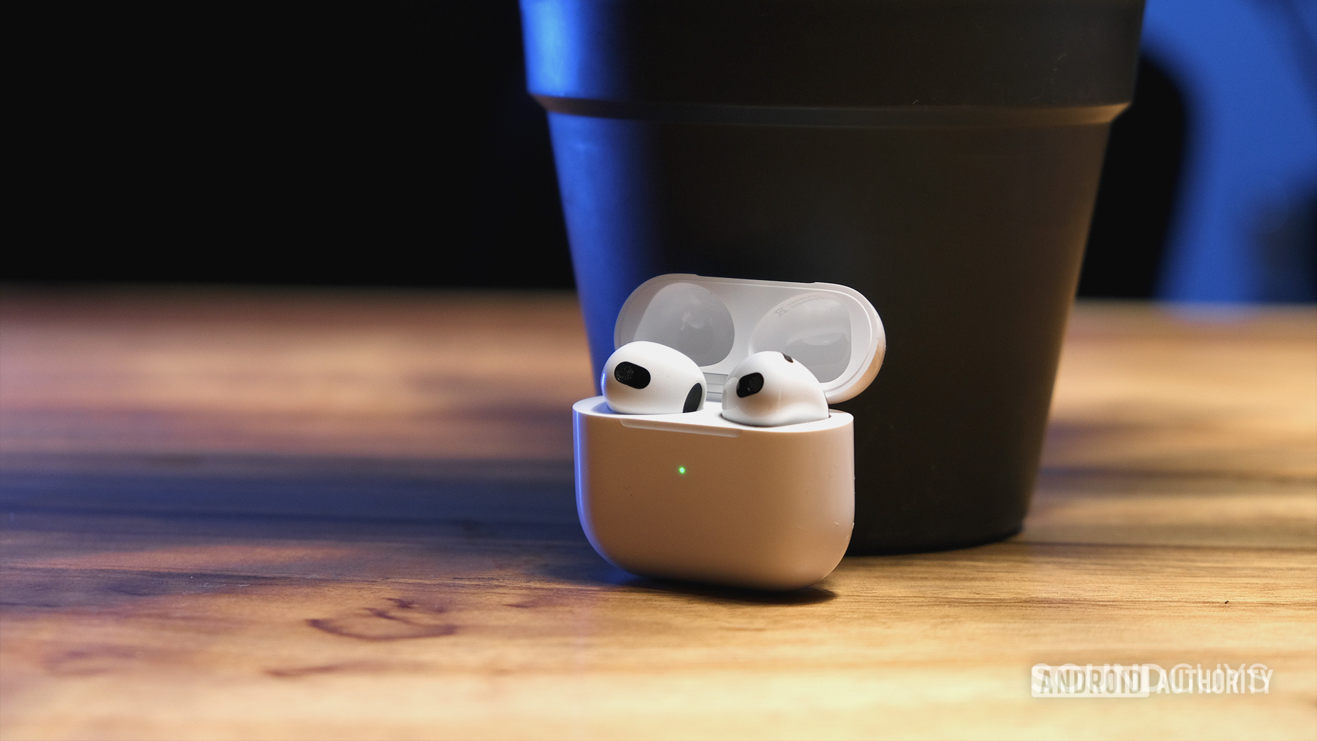 Apple Airpods（第3代）开放式盒子持有耳塞并坐在木材表面上。