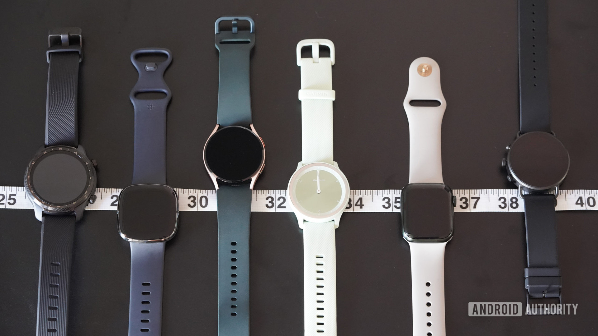 各种智能手表，包括Apple Watch系列7，Galaxy Watch 4，Garmin Vivomove Sport以及沿尺寸胶带并排休息。
