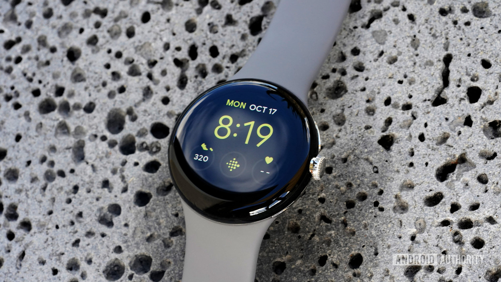 Google Pixel手表放在熔岩岩石上，显示带有Fitbit快捷方式的实用程序表面。